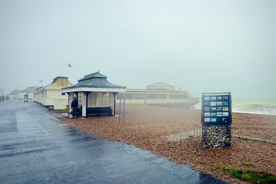 worthing seafront in wind and rain, exhibition boards in foreground showing photographs, pier visible in background