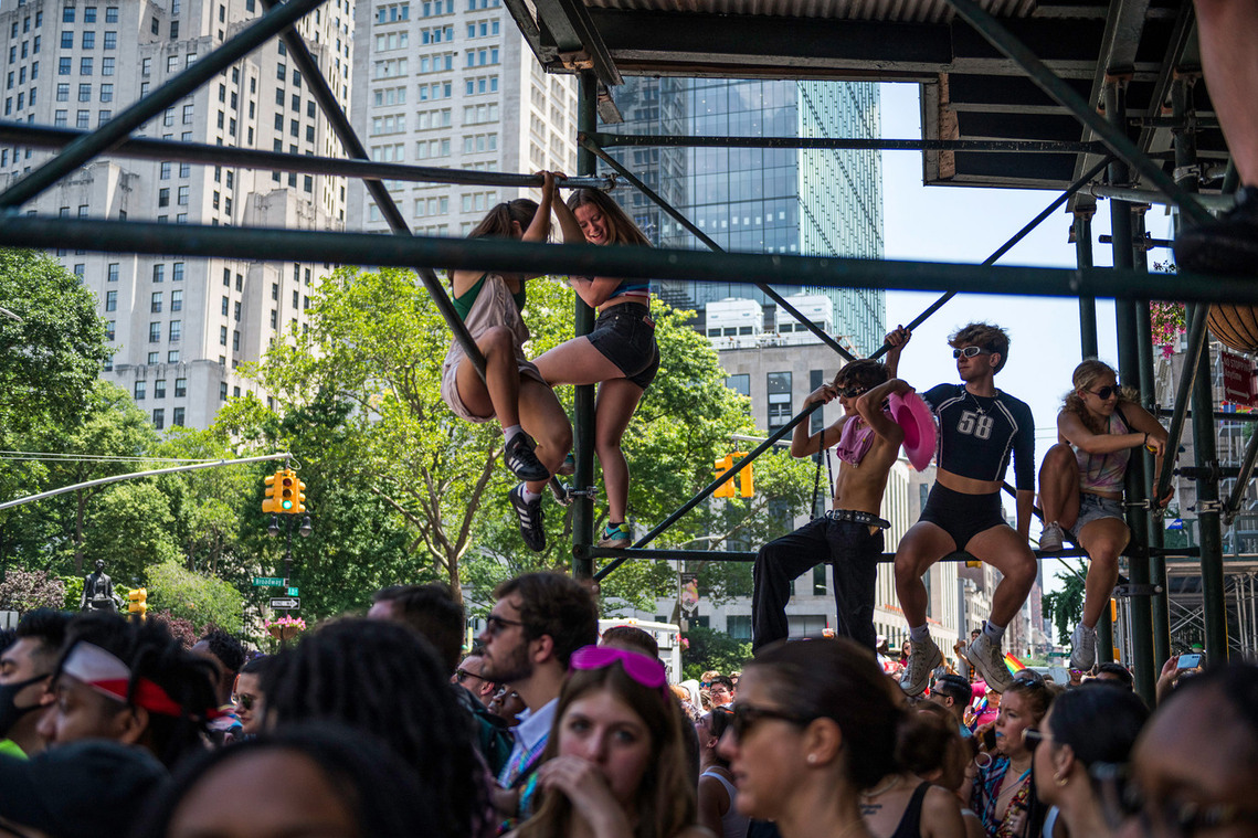 Young people sat on scaffolding in New York City watching pride march
