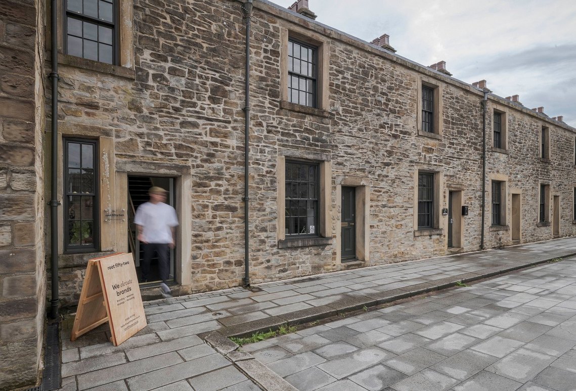 Exterior view of Root Fifty-Two's creative agency office in Burnley, showing a row of historic stone buildings with a staff member blurred in motion near the entrance, highlighting the agency's canal-side location