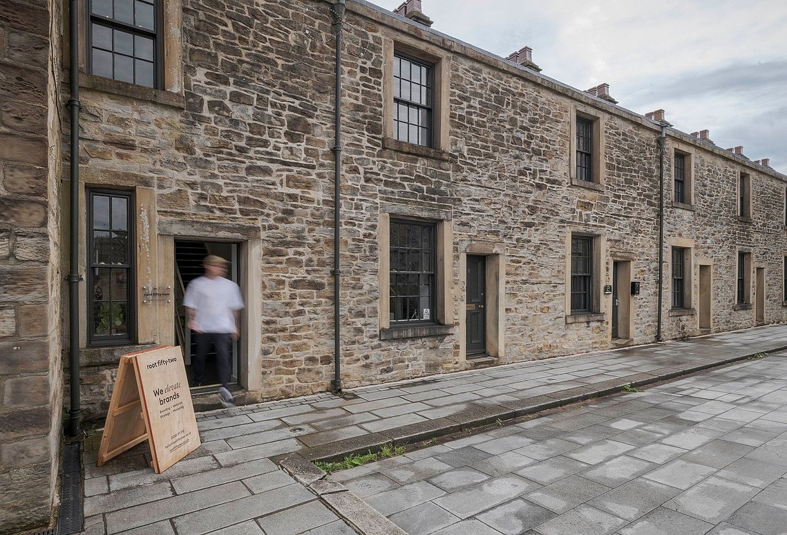 Exterior view of Root Fifty-Two's creative agency office in Burnley, showing a row of historic stone buildings with a staff member blurred in motion near the entrance, highlighting the agency's canal-side location