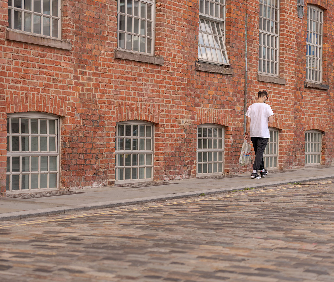 Manchester’s Ancoats — capturing the life and energy. old mill style architecture, brickwork and man walking with sopping
