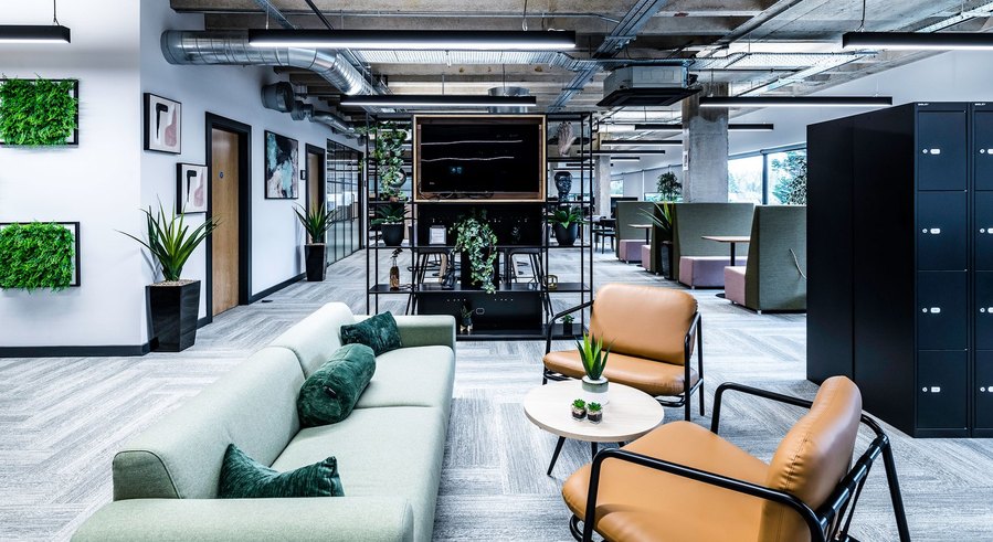 Modern office lounge with sofas, plants, and a large screen, for a relaxed working environment.