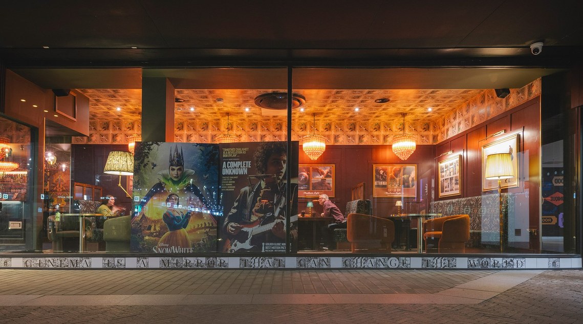 exterior photo of cinema window, with movie poster visible and people sat in dining booths