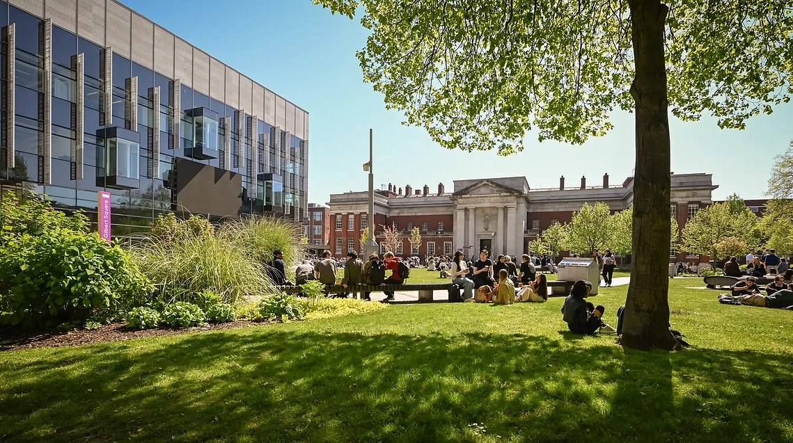 Students seated in a sunny campus courtyard with architectural facades behind them.