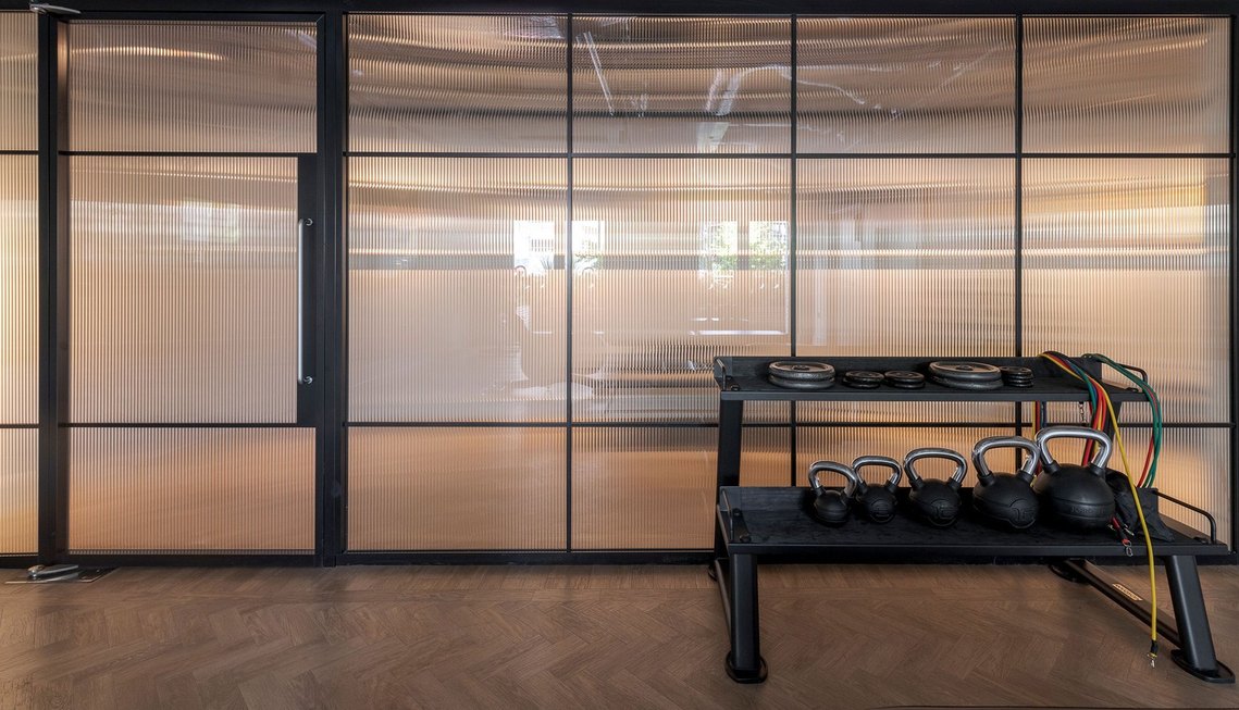 Modern gym with frosted glass walls and kettlebells on rack.