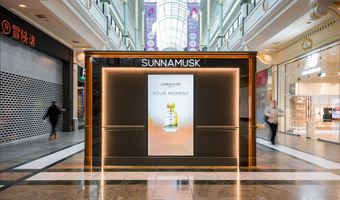 premium fragrance kiosk in middle of shopping mall with shoppers walking past