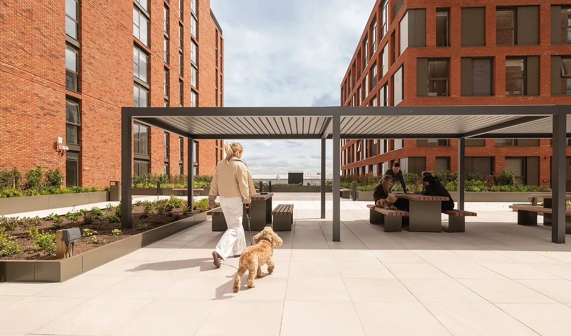 Resident walking her dog past the pergola in Podium Gardens, Old Trafford, Manchester.