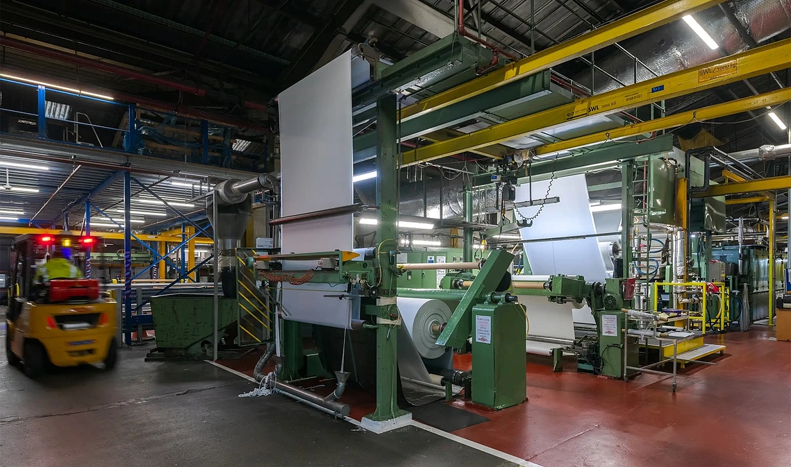 Industrial interior photography showing vintage machinery and large rolls of vinyl-coated fabrics inside a manufacturing facility.