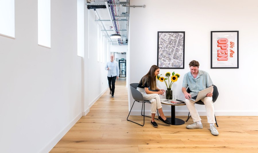 Two individuals sitting by a table in a modern hallway with art on the wall.