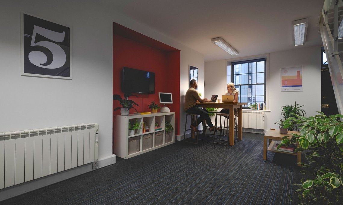 Two team members of Root Fifty-Two working together in a bright and modern open-plan office, surrounded by greenery and minimalist decor, showcasing the agency’s collaborative environment.