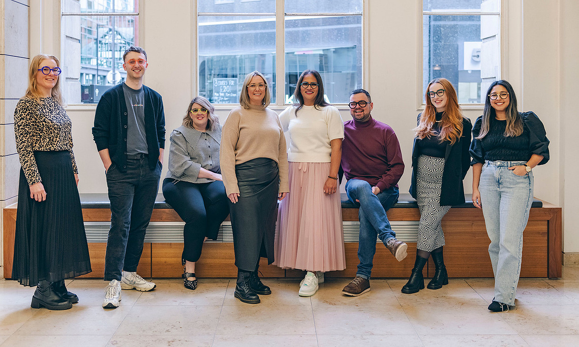 a group shot of team of staff, relaxed poses in front of a window in white interior space