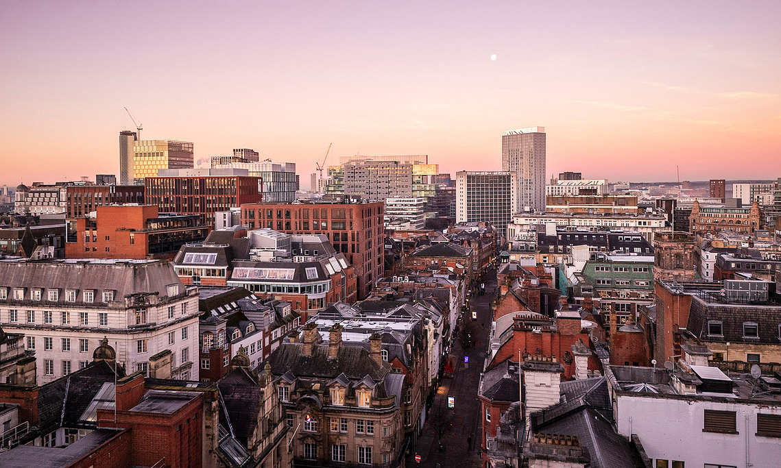 drone photography shows manchester skyline at dusk with moon in sky