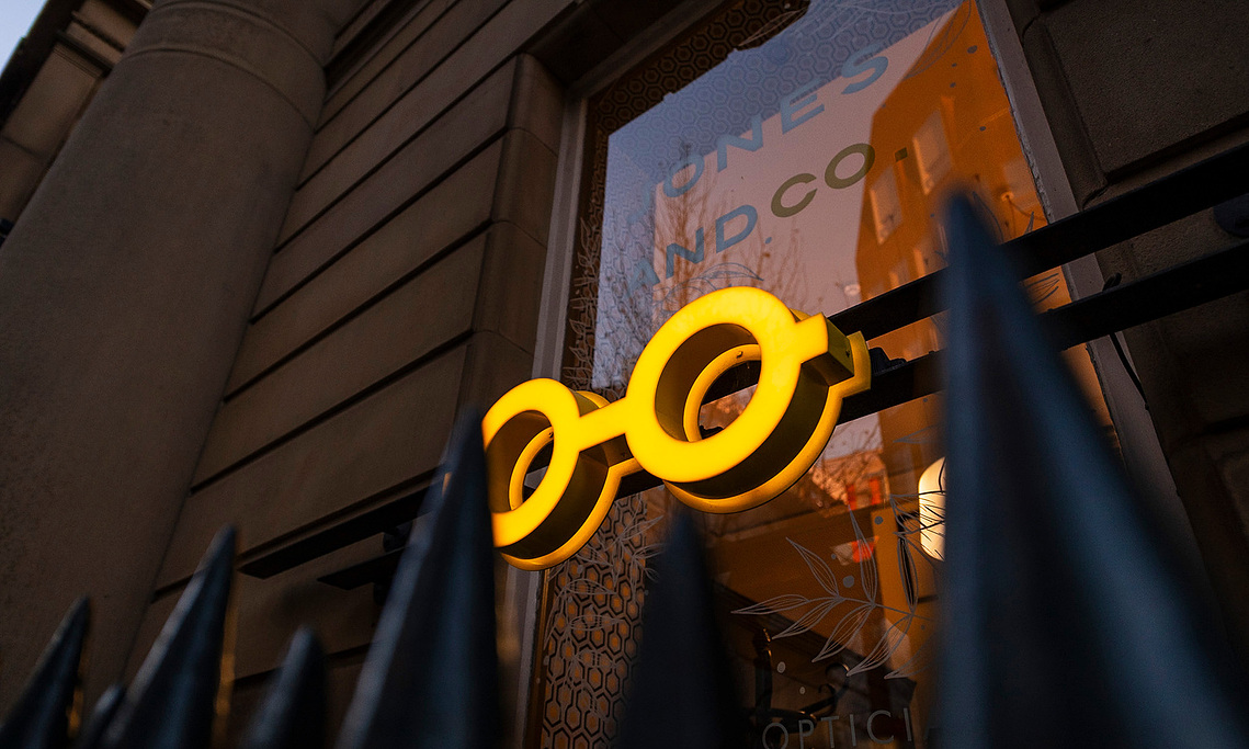 glasses logo glows outside window at dusk