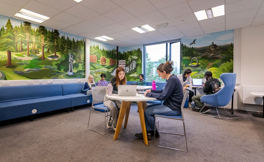 student lifestyle photography, group of students sat at different tables in a breakout space