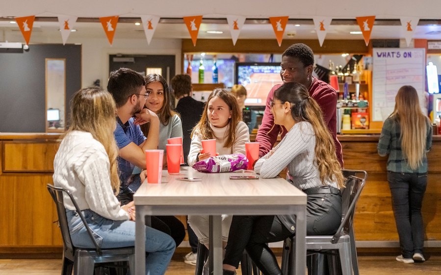 student lifestyle photography, group of students huddle around table in a bar