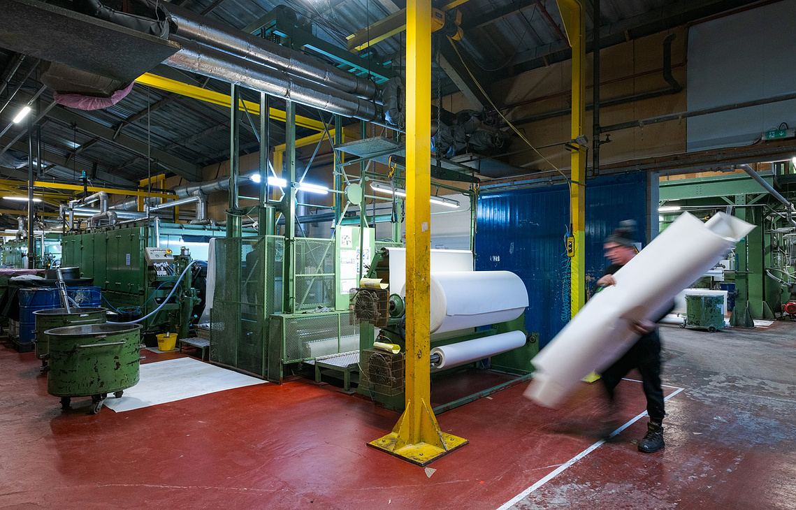 Documentary manufacturing photography capturing a factory worker carrying large roll to machinery