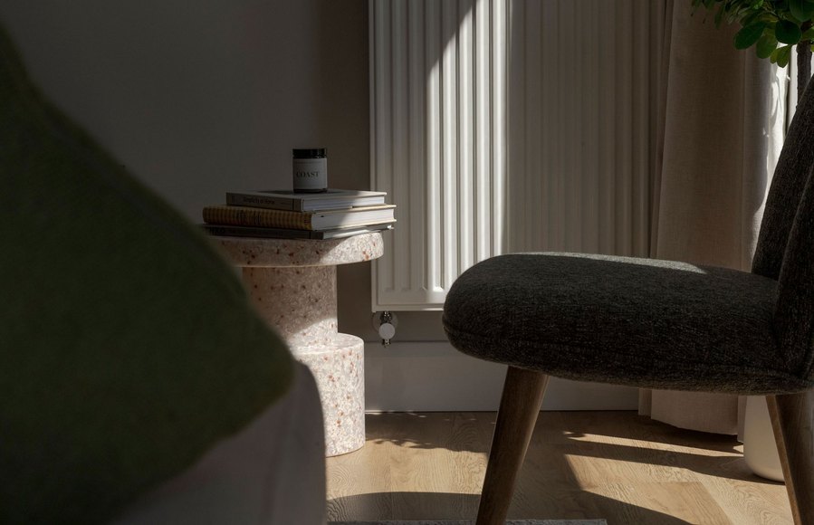 Sunlit modern room with a terrazzo side table holding books and a candle, flanked by two chairs.