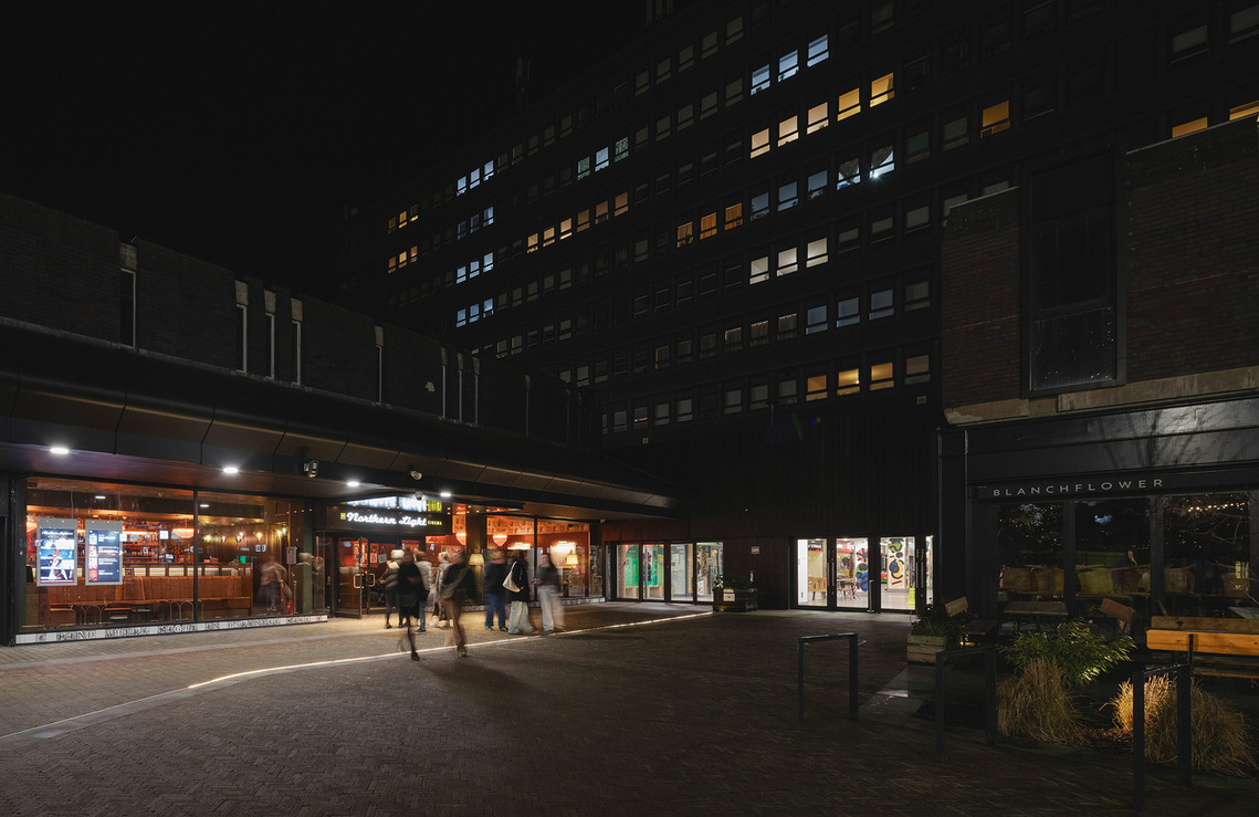 exterior architectural photography of a cinema at night, light spills from windows and people walk toward the door. tower with lights in background 