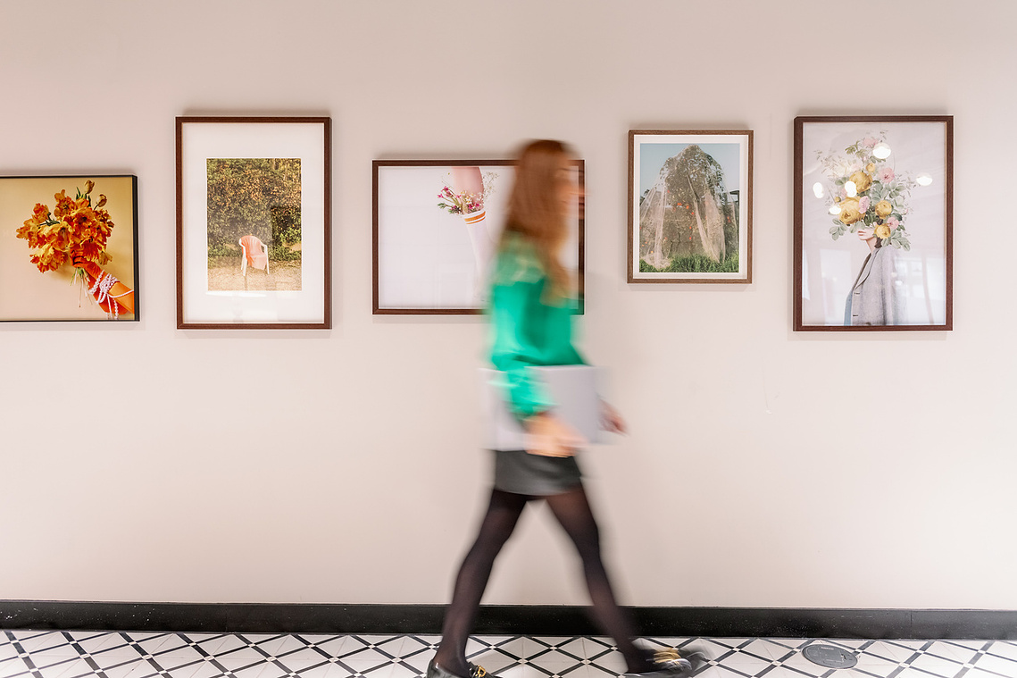 Relaxed workplace interaction candid marketing imagery, worker with laptop walks past pictures on wall