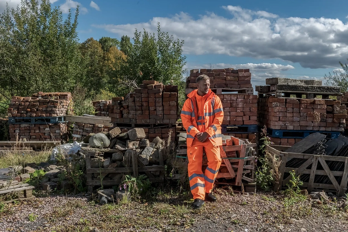 Product lifestyle photography of Blackrock Workwear on location, model in hi-vis wear leans on worksite location