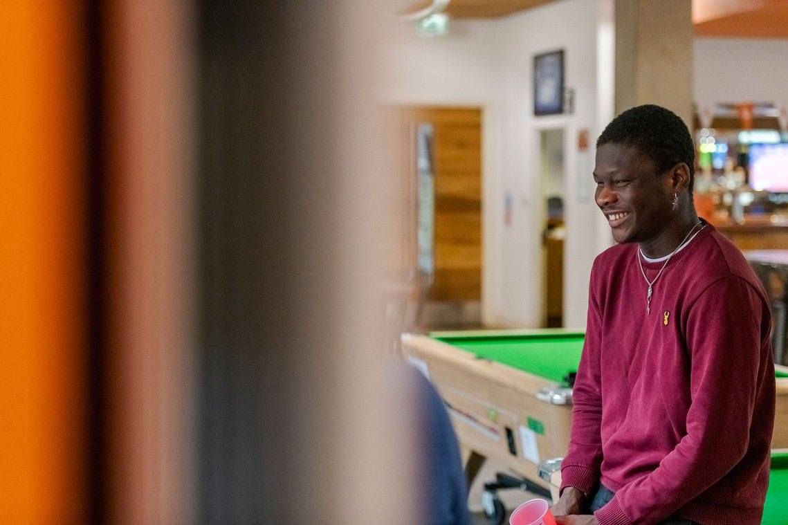 Student sits on edge of pool table and laughs with others not in the frame.