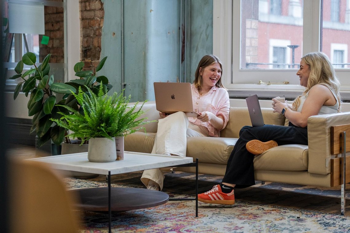 commercial lifestyle photography showing staff in a workplace, candid photograph showing team members sat on a sofa discussing work on a laptop