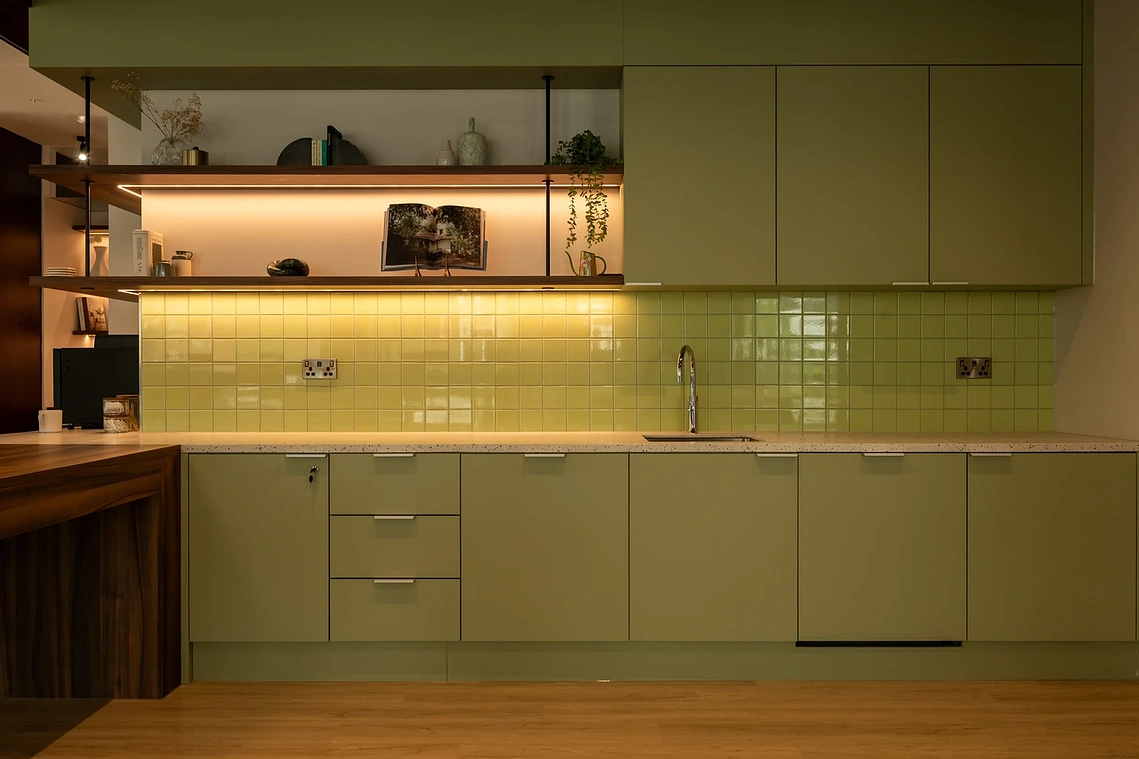 Sage green residents' kitchen with tiled splashback and open shelving at Podium, Old Trafford, Manchester.