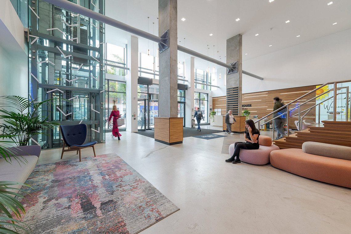 Commercial interiors photographer capturing workspace design details for Clockwise brand photography. Atrium style entrance to building with multiple people passing through the frame 