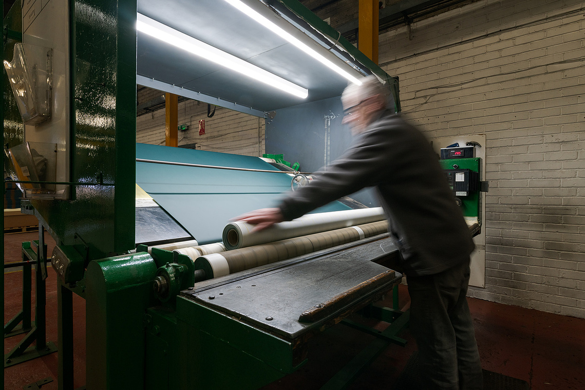 Documentary manufacturing photography capturing a factory worker operating machinery during the Ambla fabric production process. paper rolls