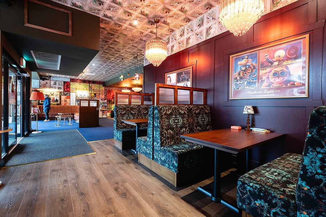 wide architecture photography of cinema lobby with seating booths and colourful walls. person in background looking at poster