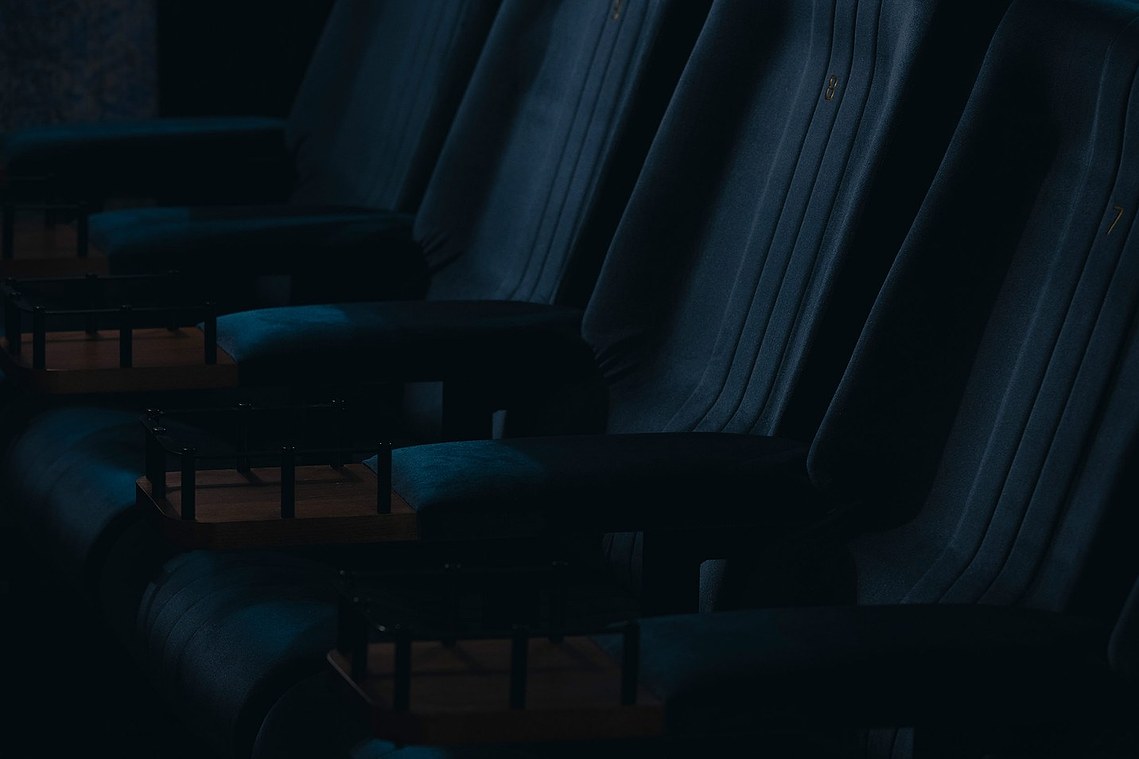 cropped photo of cinema seats, blue  plush velvet fabric and deco style drink holders, moody lighting