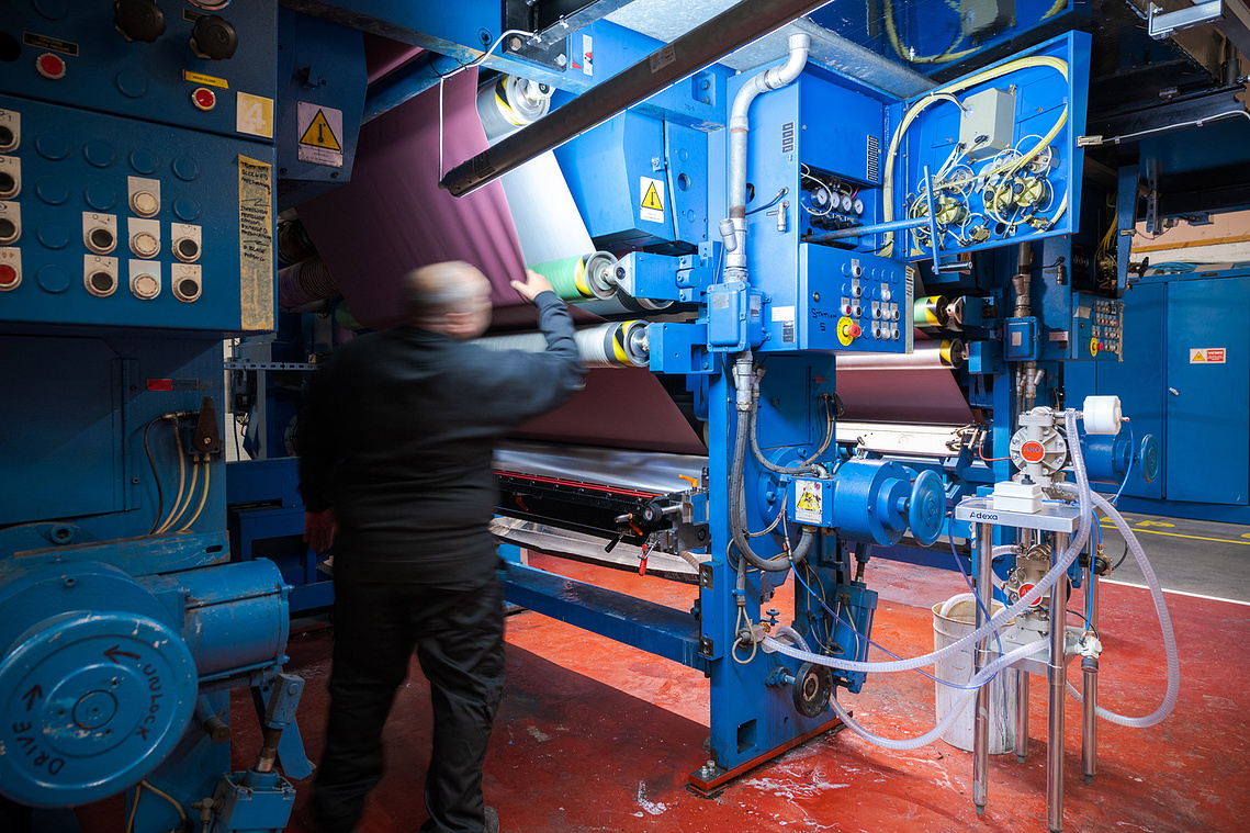 Documentary manufacturing photography capturing a factory worker operating machinery during the Ambla fabric production process