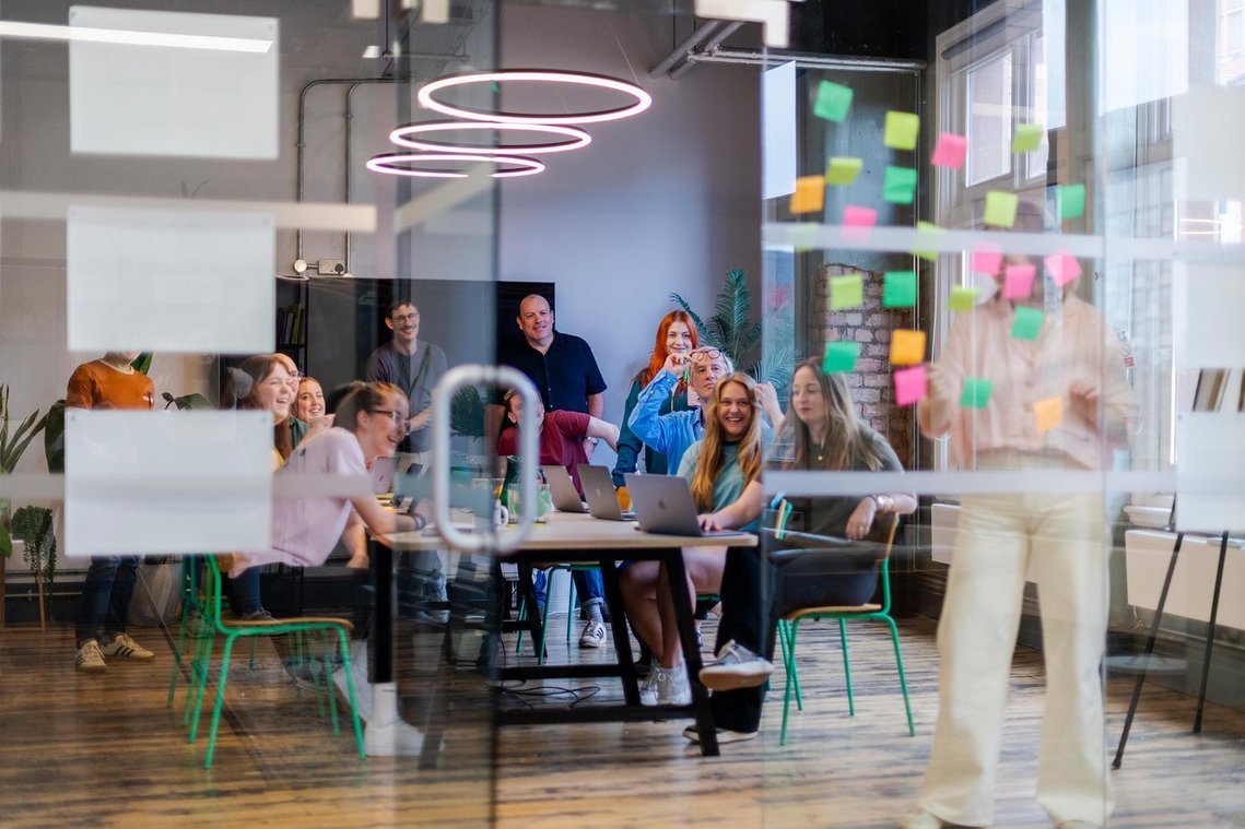 commercial lifestyle photography showing staff in a workplace, team meeting in room with large table, notes stuck on window wall