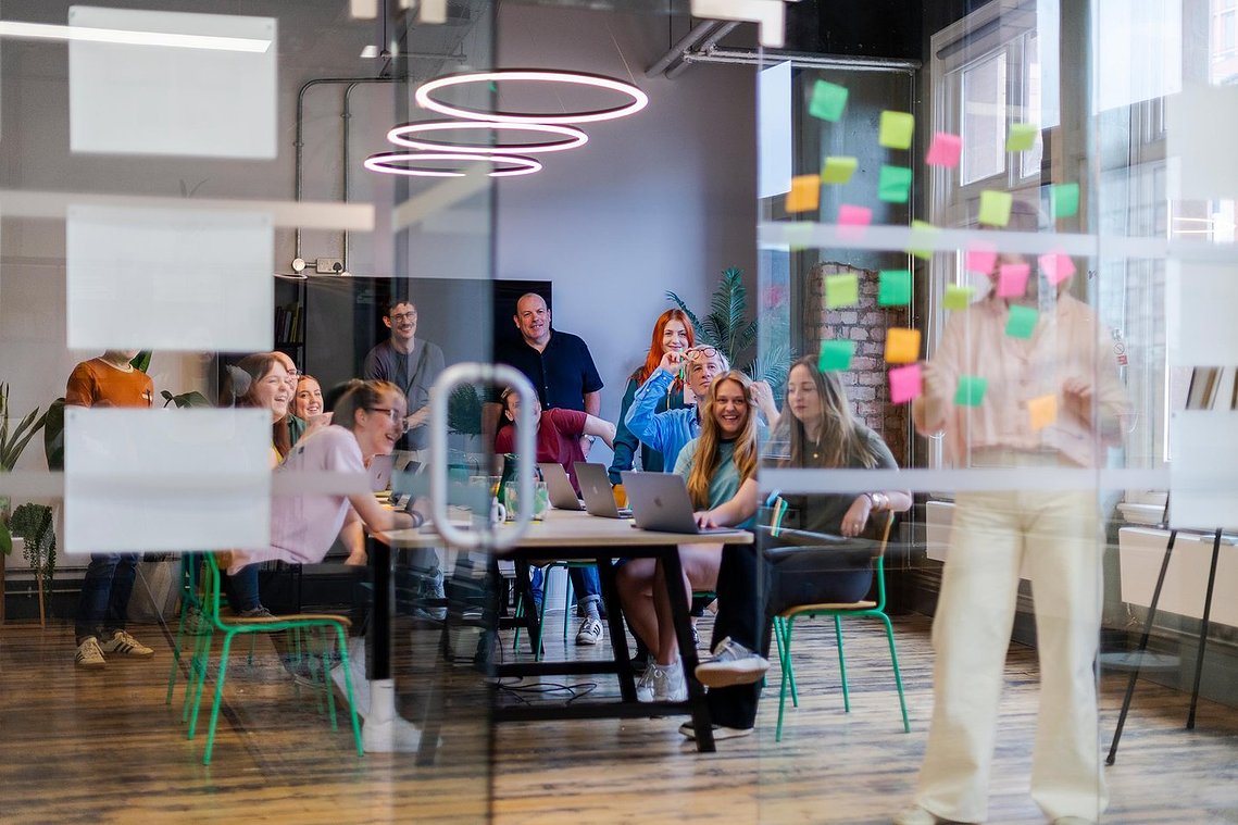 commercial lifestyle photography showing staff in a workplace, team meeting in room with large table, notes stuck on window wall