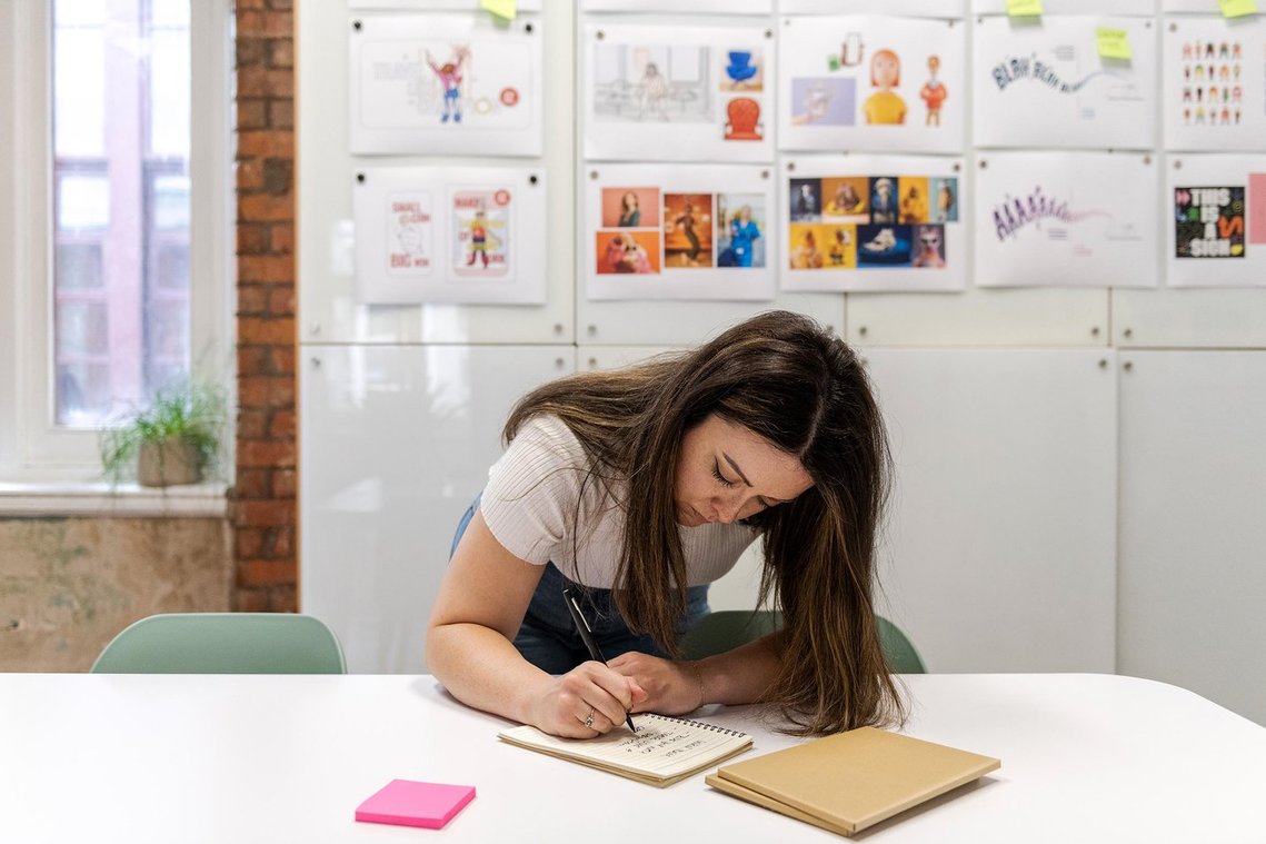 commercial lifestyle photography showing staff in a workplace, team member leans on table and writes in pad