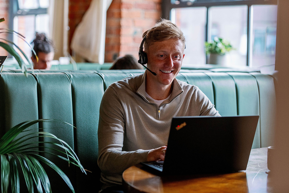 Commercial lifestyle photography. Man sat in workspace with laptop and headset. Professional.