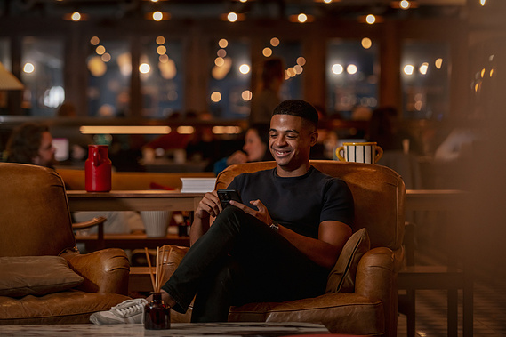 Commercial lifestyle photography, smiling relaxed worker sits in armchair in warm tones
