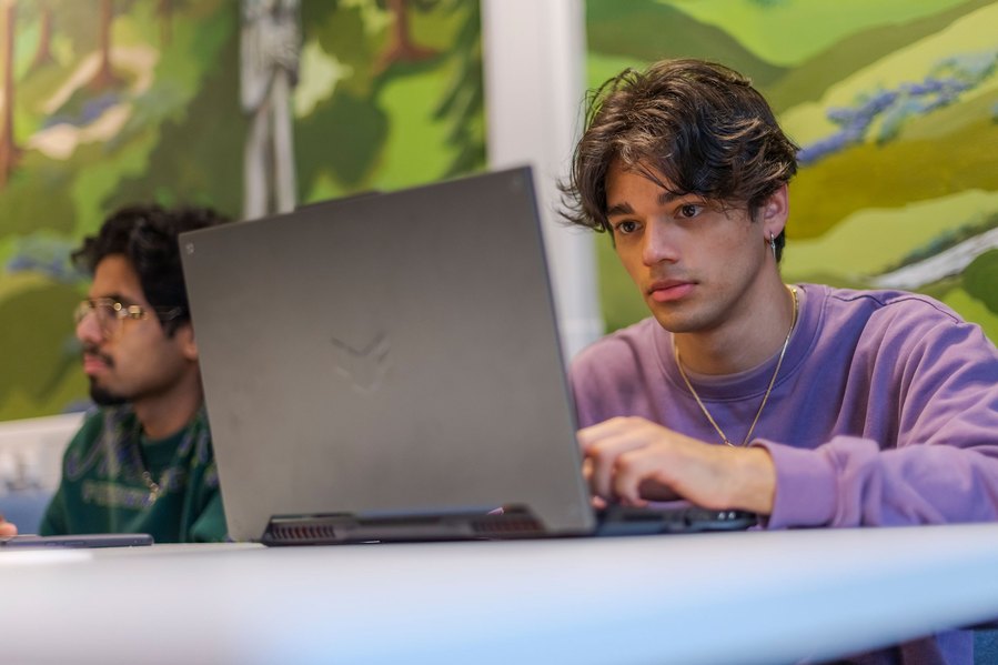 student lifestyle photography, young male sits working on a laptop, bright green mural on wall behind