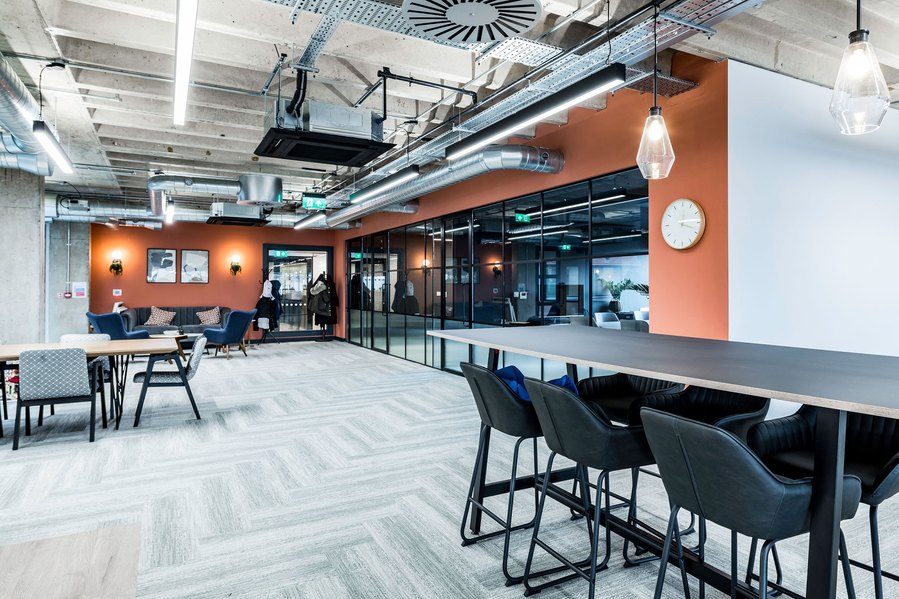 Modern office interior with seating area, long table, chairs, and exposed ceiling.