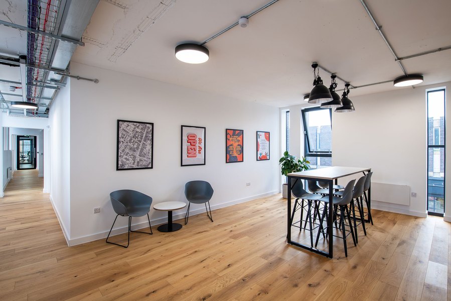 Modern office space with wooden floors, artwork on walls, and a high table with chairs.