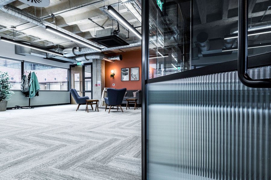 Modern office lounge with chairs, artworks on walls, and exposed ceiling ducts.