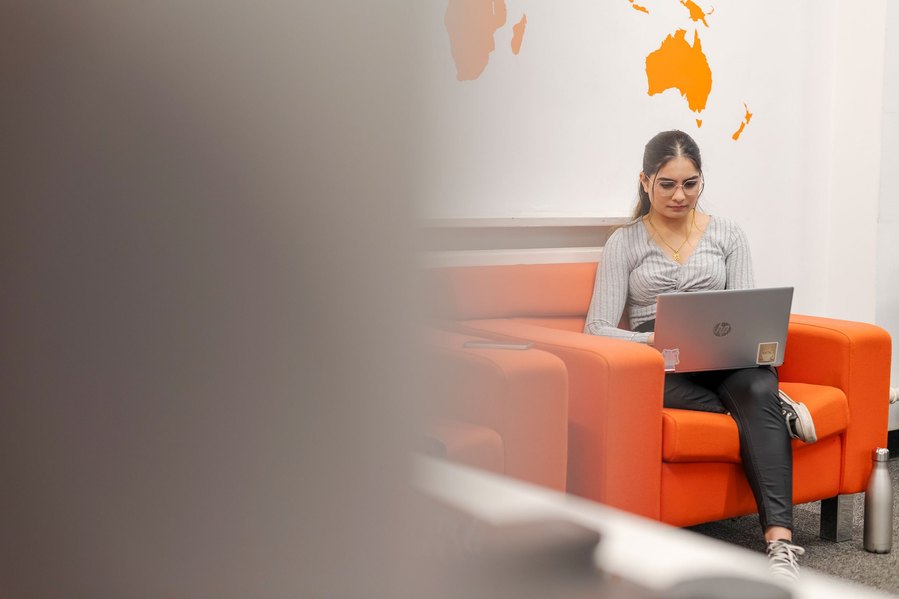 student lifestyle photography, girl sits working on a laptop, orange chair