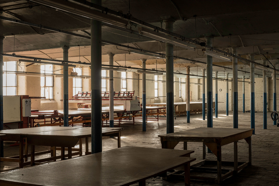 Empty industrial room with tables, columns, and natural light from windows.
