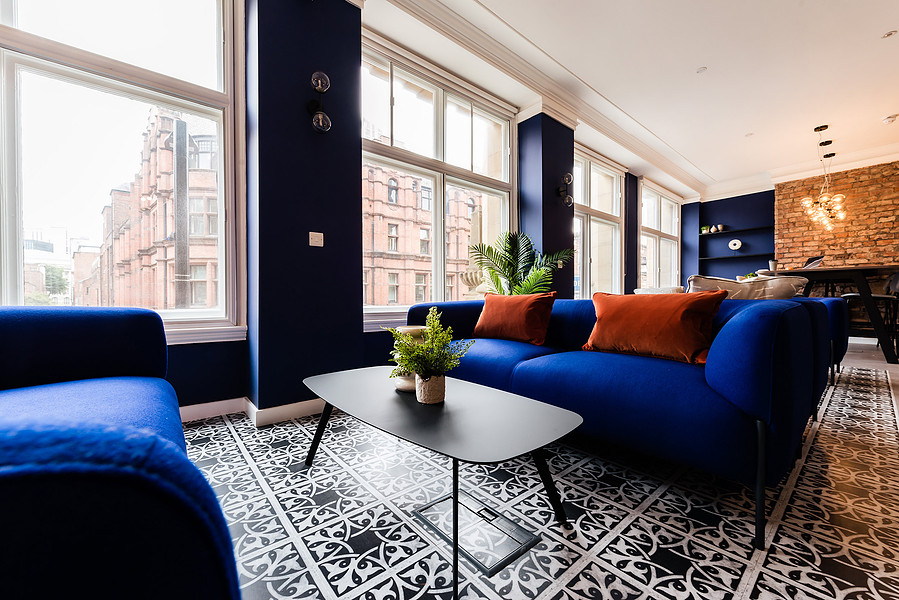 sofa and coffee table in commercial office property shared space. blue sofa with orange cushions. flowers and glasses on table