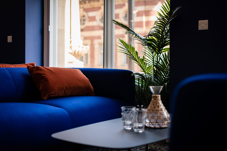 sofa and coffee table in commercial office property shared space. blue sofa with orange cushions. flowers and glasses on table
