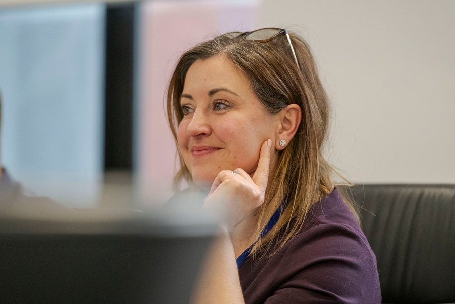 A woman with glasses on her head, sits at a desk with a thoughtful expression, embodying the essence of relaxed corporate photography.