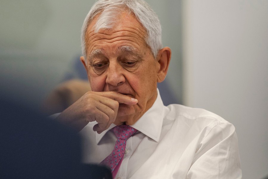 Man in a white shirt and pink tie, looking down thoughtfully with his hand on his chin, captured in a relaxed corporate photography style.
