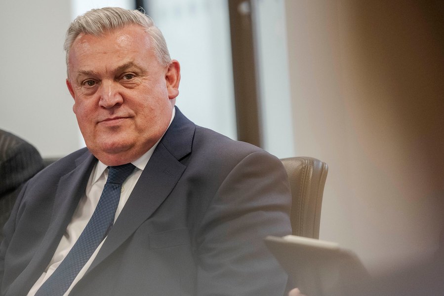 A man in a suit sits at a table in an office setting. Relaxed corporate photography captured expertly by a Manchester commercial photographer.