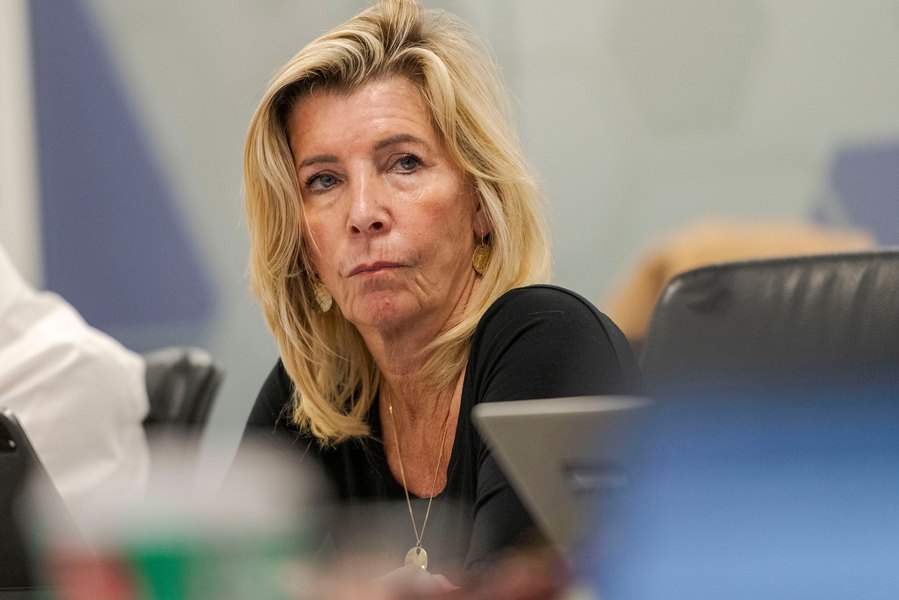 A woman sits at a table in a relaxed corporate photography setting, looking to the side with a neutral expression. Captured effortlessly by a Manchester commercial photographer.