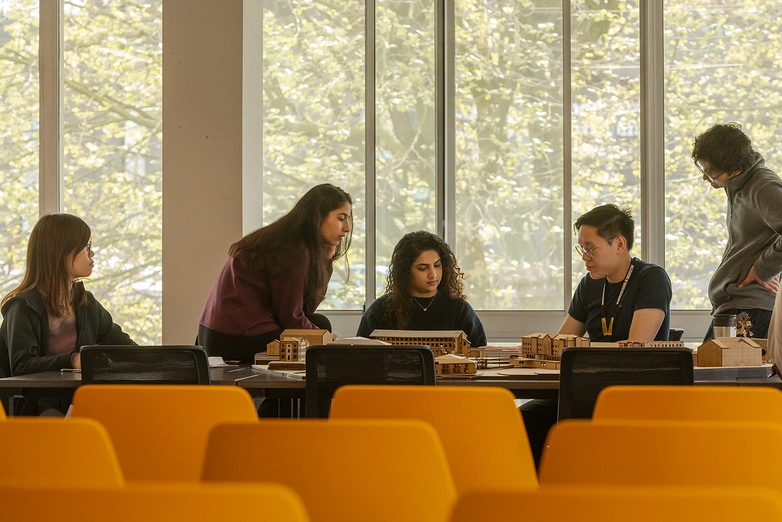 Group of architecture students collaborating over models at a large studio desk